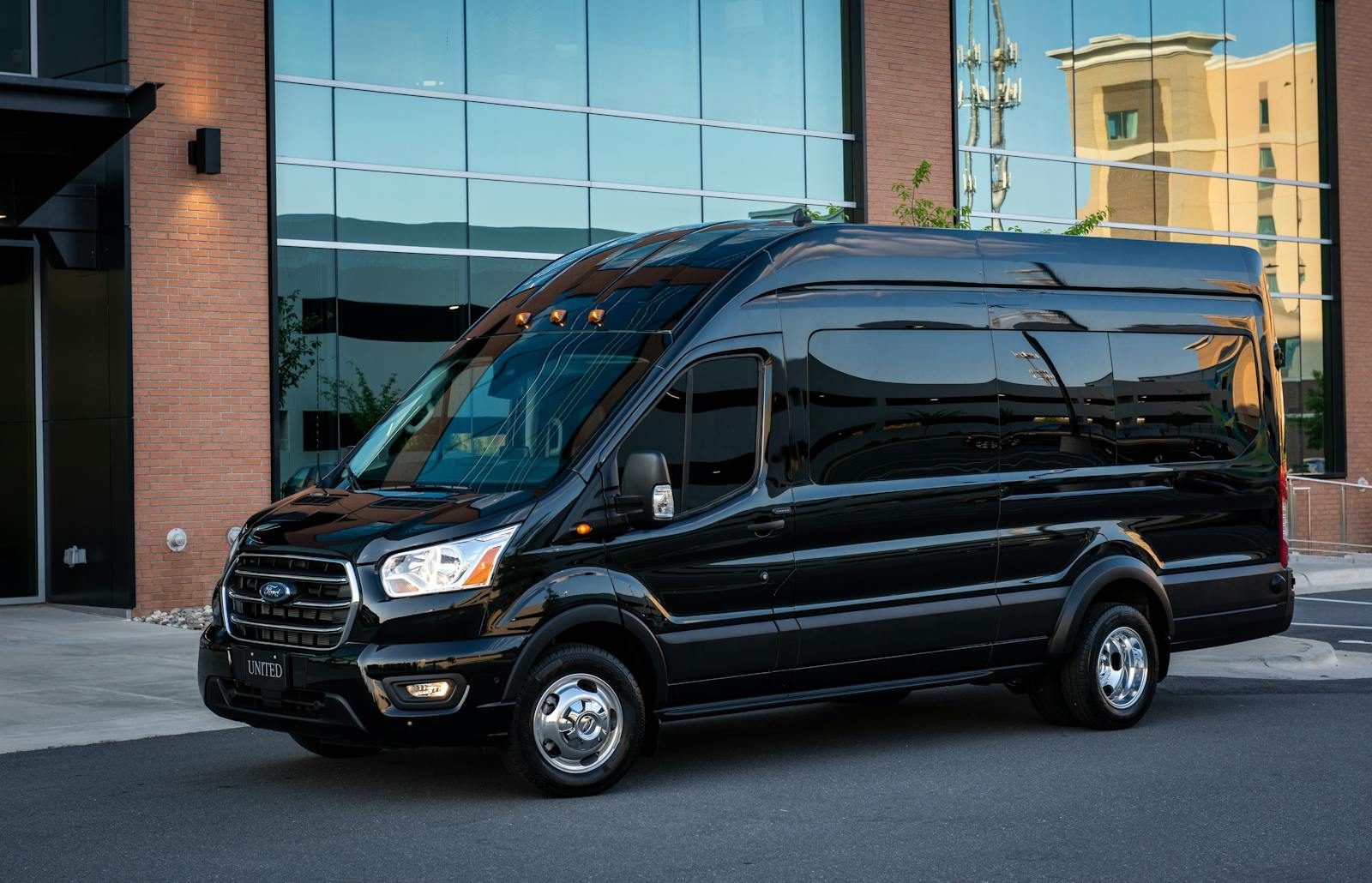 A modern black van parked outside a glass building in an urban area.